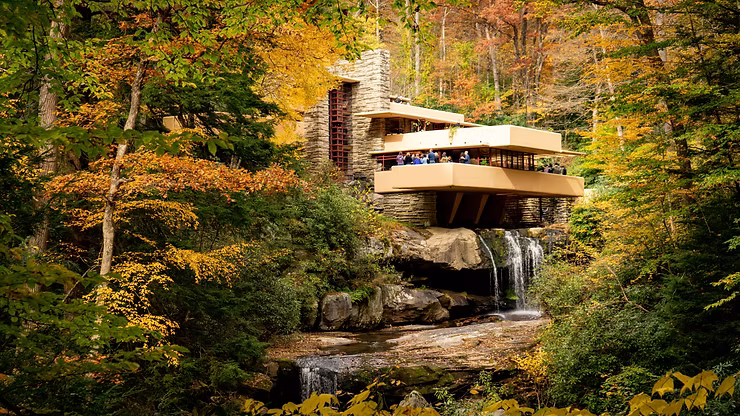 Exterior view of Fallingwater house by Frank Lloyd Wright, perched over a waterfall surrounded by lush green forest,