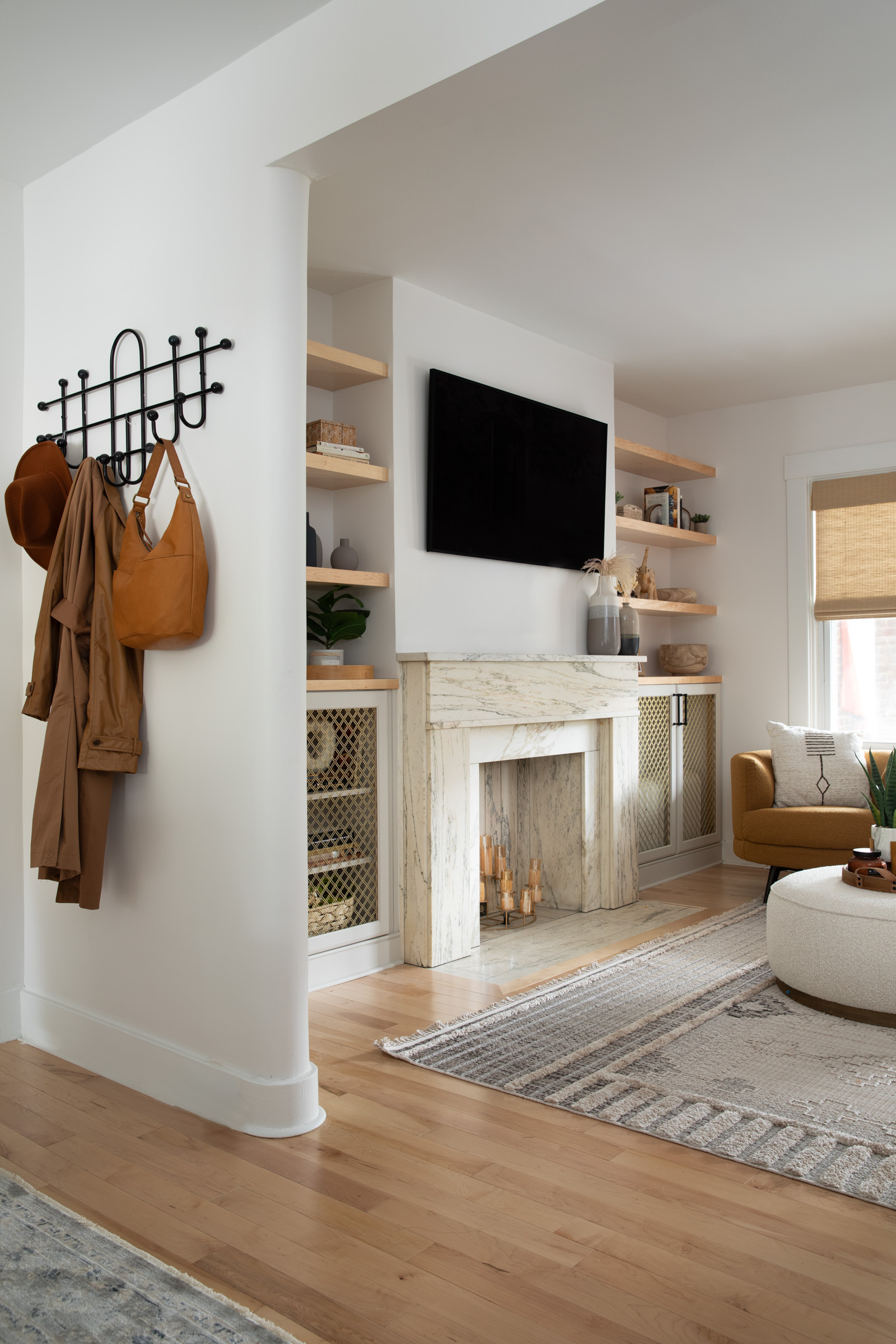 A renovated living and dining room in a historic Squirrel Hill home featuring custom built-ins with brass details, a preserved marble fireplace, layered natural textures, and curated artwork.