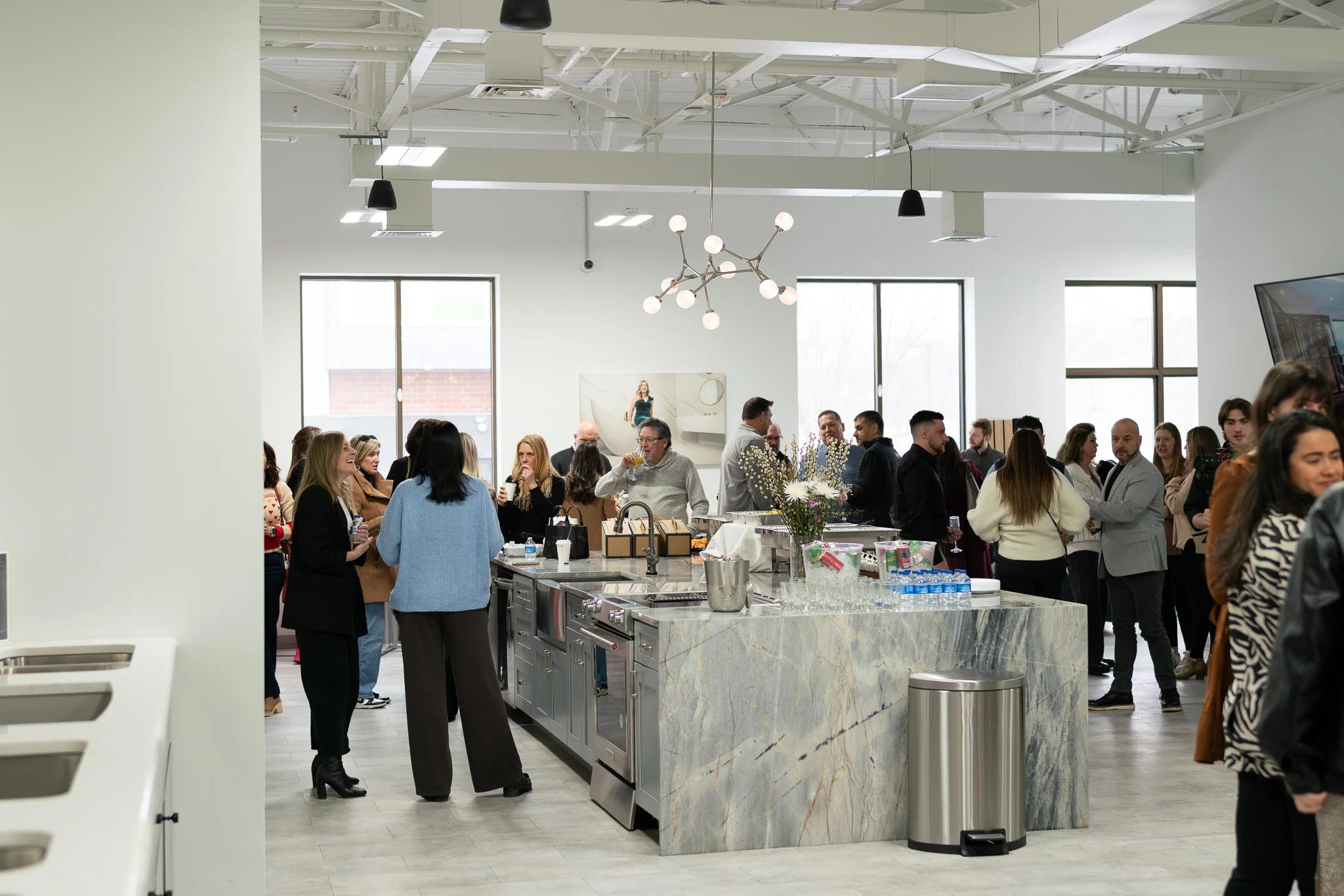 Interior designers gathered at Armina Stone showroom in Cranberry around a large granite island during a catered networking brunch, featuring a crêpe station and keynote presentation by a designer in a chartreuse velvet dress.